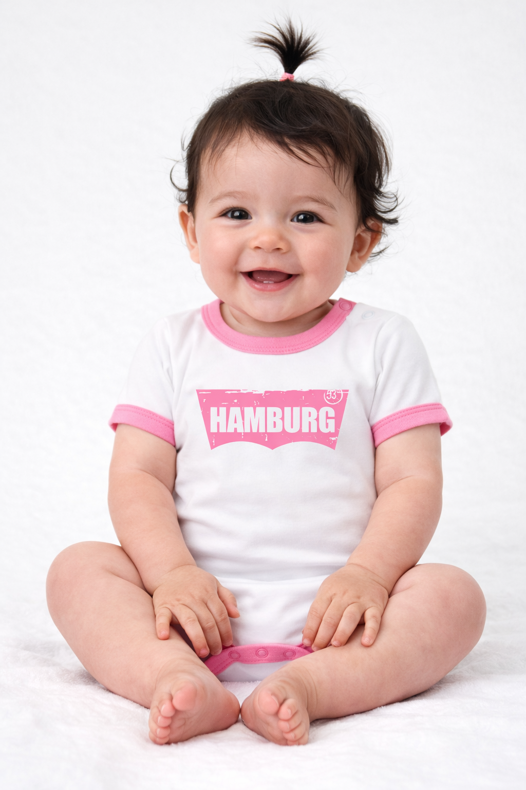 Fröhliches Baby im weißen Body mit rosa „Hamburg“ Schriftzug im Vintage-Stil, neutraler Hintergrund