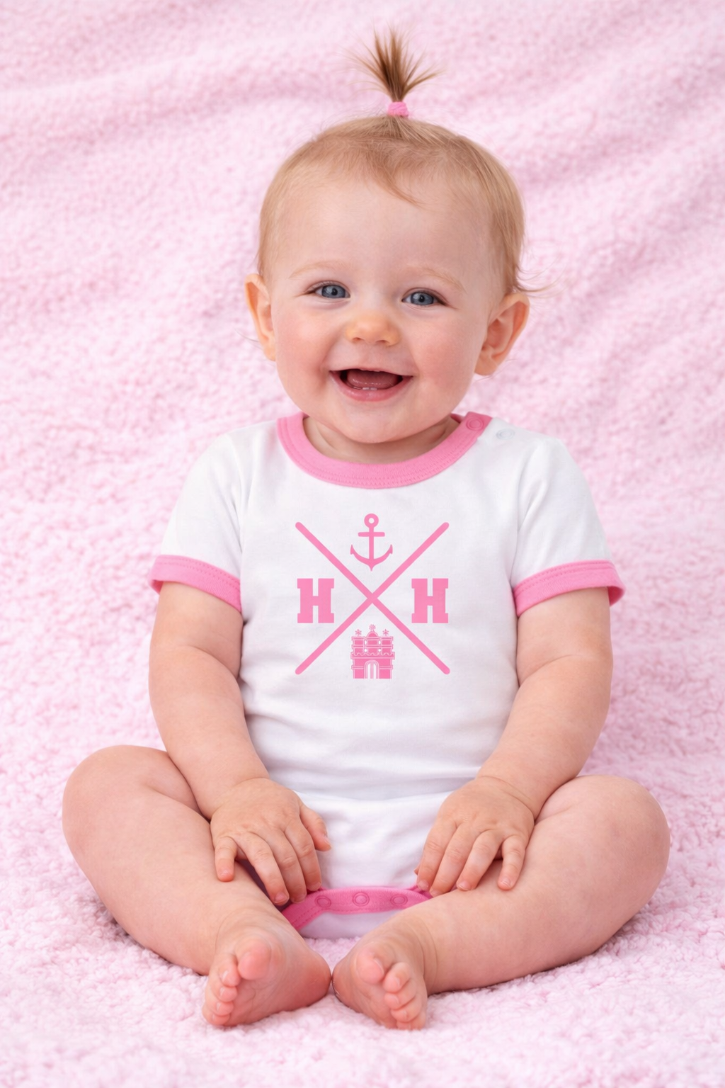 Lächelndes Baby im weißen Body mit rosa Bündchen und Hamburg HH Anker Design, sitzt auf rosa Hintergrund