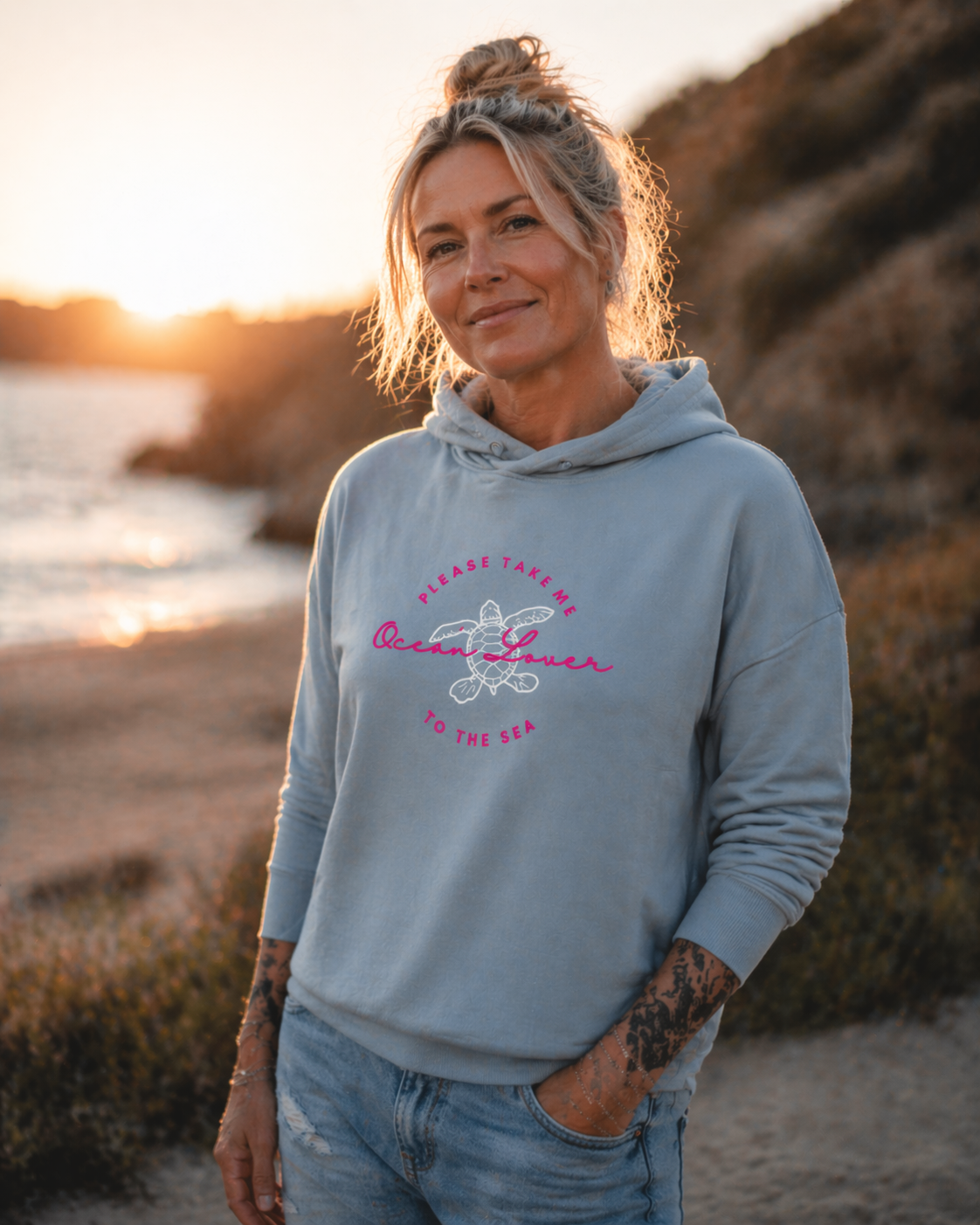 Ocean Lover Hoodie Strand Look: Hellblauer Damen Hoodie mit pink-weißem Meeres-Print, getragen bei Sonnenuntergang am Strand – stylischer Beach Hoodie für Urlaub und Freizeit.